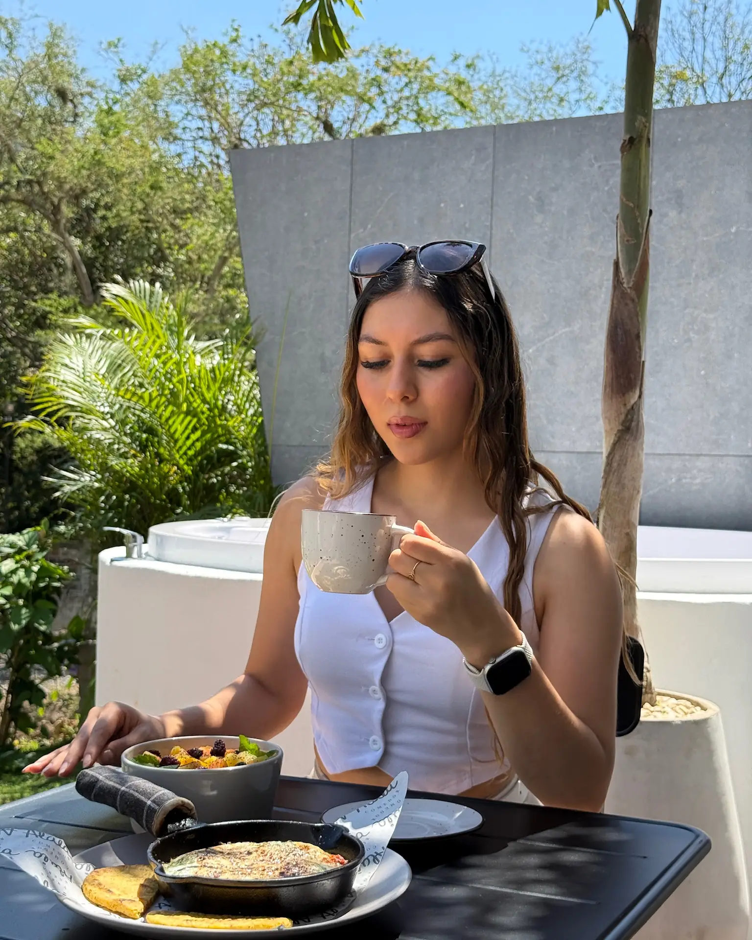 Huésped desayunando en la terraza de una cabaña doble, con el jacuzzi y el jardín detrás