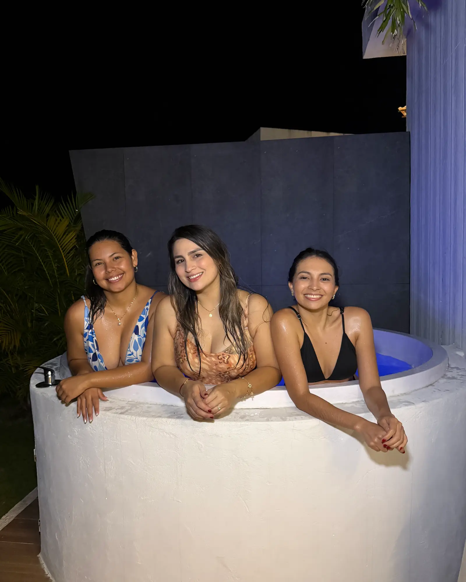 Tres amigas sonríen dentro del jacuzzi iluminado de una cabaña, de noche